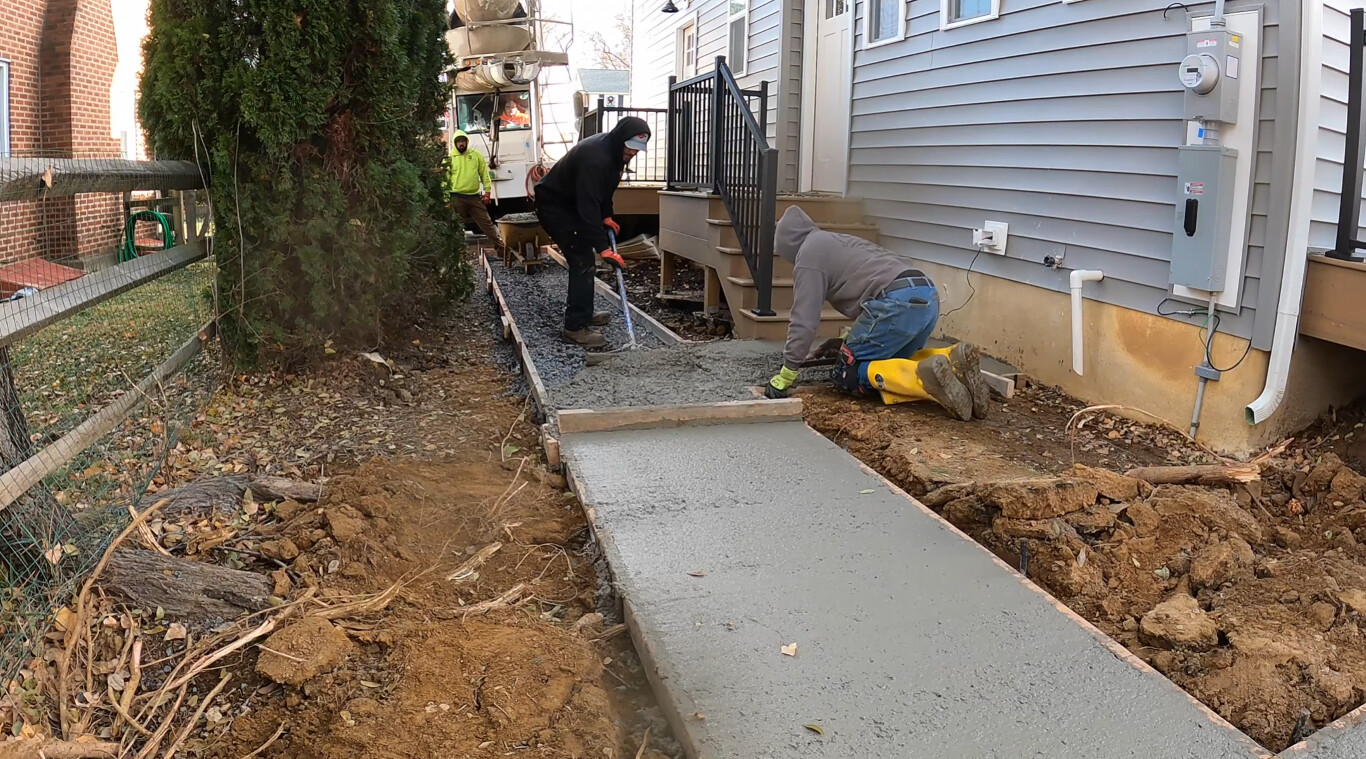 Workers finishing concrete sidewalk installation next to residential home